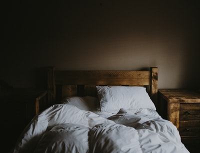 白色床上被子集和棕色木质床框棕色木质床头柜旁边
